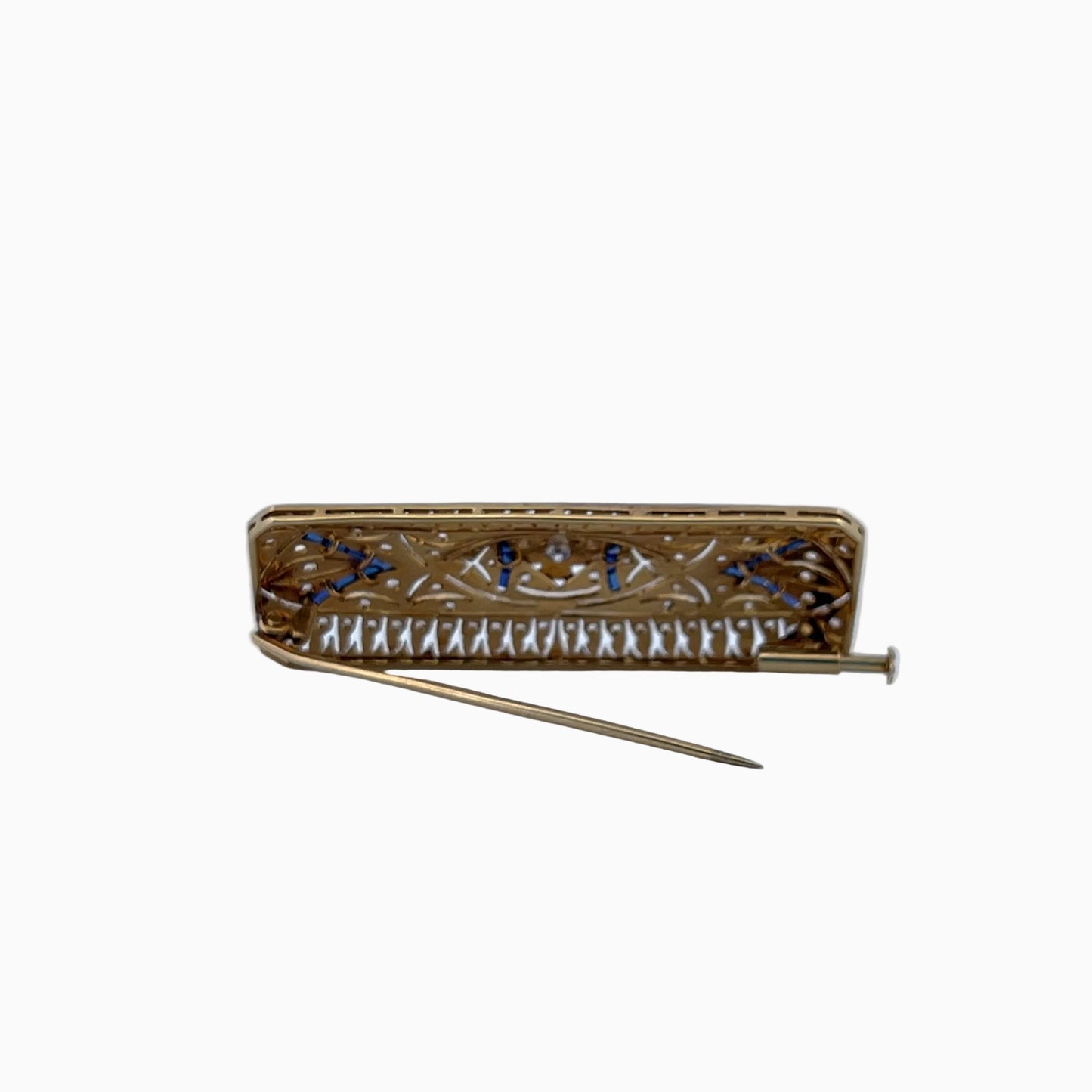 A vintage gold-toned rectangular pin with intricate cutout detailing, blue stone accents, and a row of small white stones along the lower edge, shown on a light blue background.